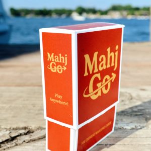 MahjGo Chinese mahjong playing card box showcased outdoors on a rustic wooden dock overlooking a lake.